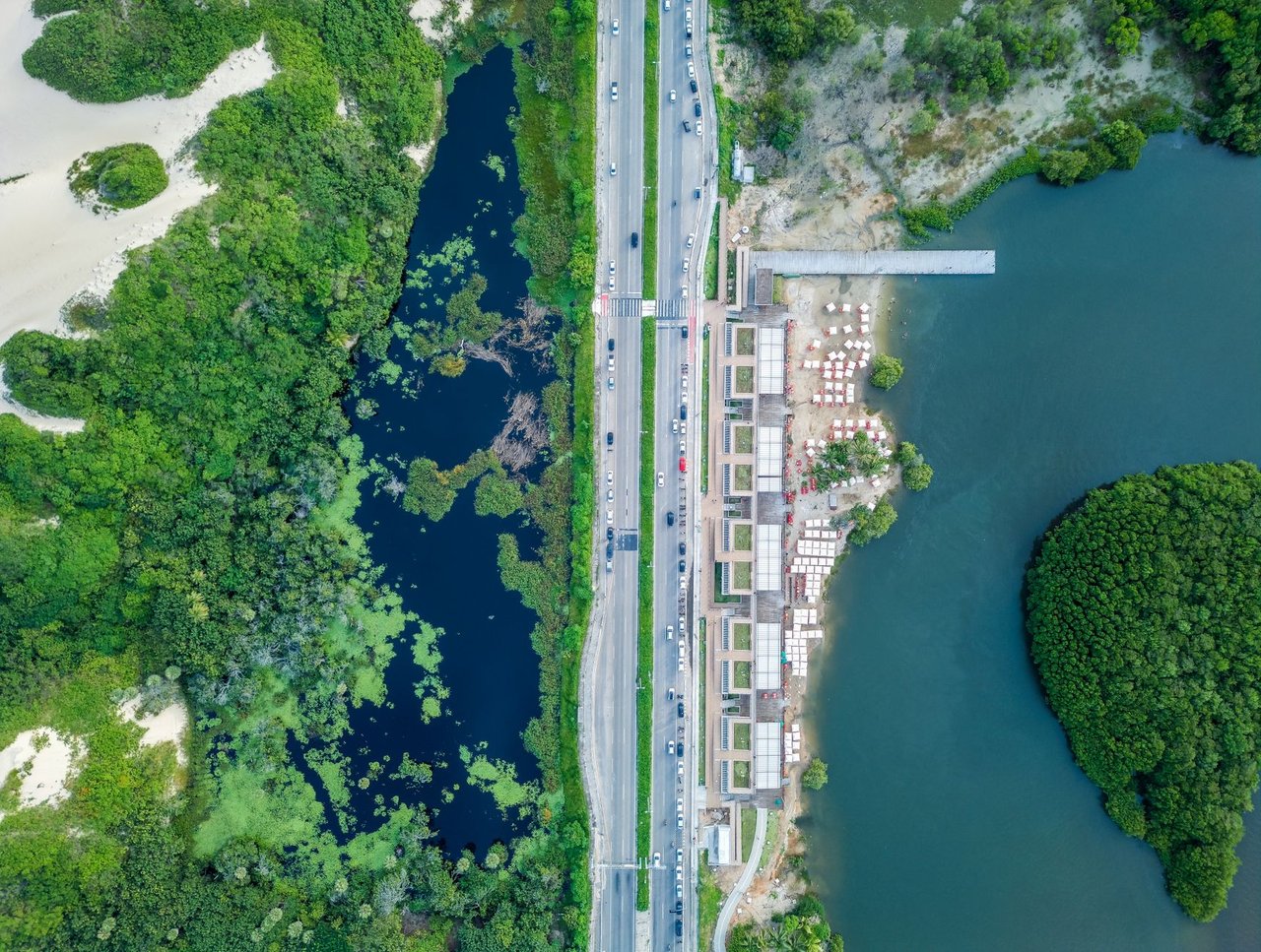 Vista aérea de trecho urbanizado do litoral de Fortaleza, com avenida, áreas verdes e a faixa de praia.