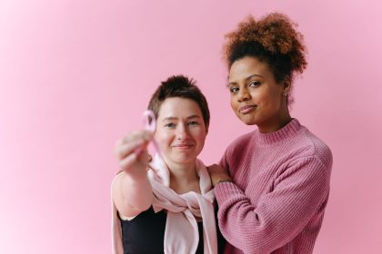 Duas mulheres se abraçam; uma delas segura uma fita rosa, símbolo de conscientização sobre o câncer de mama.